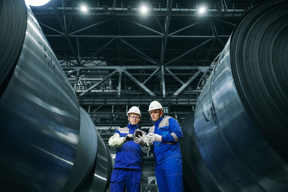 Two professionals inspecting steel coils at a plant